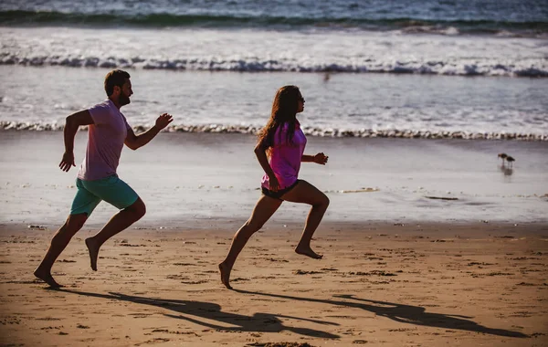 Pár jich běhá na pláži. Sportovec a sportovkyně běží společně u moře. — Stock fotografie