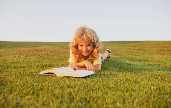 Grabben läste bok i parken. Leende roligt barn i t-shirt har kul att läsa bok i parken. — Stockfoto