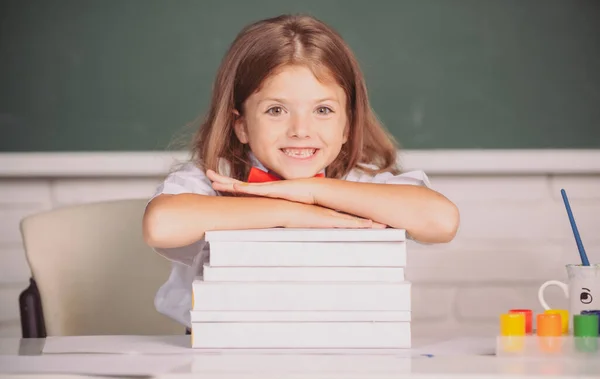 机の上に座った笑顔の少女が教室の本を手にしている。教育過程. — ストック写真