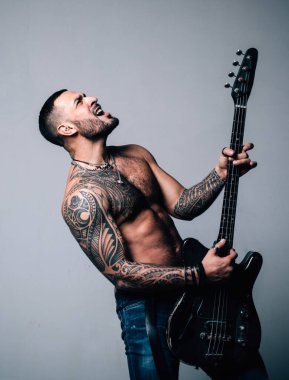 Elektro gitarla rock-n-roll çalan etkileyici genç bir adam. Elektro gitarlı heyecanlı seksi adam. Sahne ve bando enstrümanları. Güçlü, kaslı, kaslı adam. Müzik konsepti. Gitar çalan adam