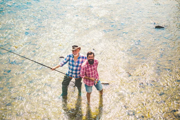 Balıkçıların arkadaşları ve ganimet alabalıkları. Baba oğul balık tutuyor. Nesiller boyu nehirde balık tutan adamlar. — Stok fotoğraf