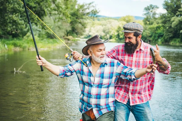 Twee mannen die vissen. Vliegvissen hengelaar maakt gegoten, staande in de rivier water. Oude en jonge visser. Gelukkig opgewonden man vrienden. — Stockfoto