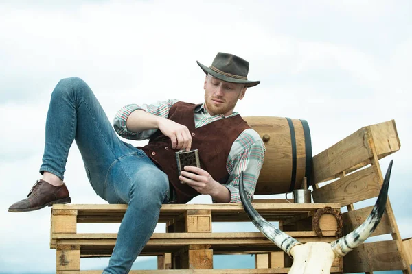 Farmer cowboy wearing hat. Western life. American country male portrait. Farm owner worker in countryside on farm or ranch. Attractive man with whiskey or brandy. — Stock Photo, Image