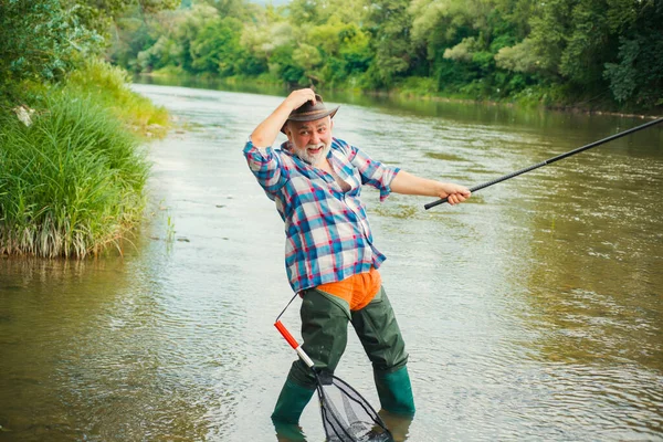 Emozionato pescatore uomo anziano con canna da pesca, filatura bobina sul fiume. Vecchio cattura pesce, tirando canna durante la pesca sul lago. — Foto Stock