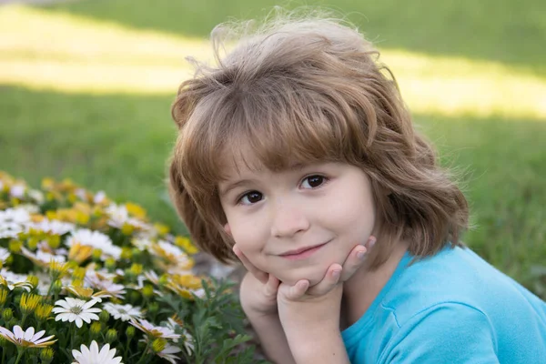 Pojken luktar blommor på en grön bakgård. En förtjusande unge på en sommaräng och doftande blommor. Sommarnöje för familj med barn utomhus i en vacker vårträdgård. — Stockfoto