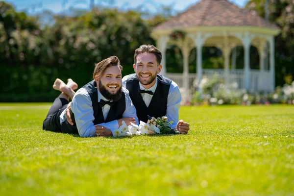 Портрет щасливої пари геїв, які паруються на траві в день весілля. Весілля веселе. Весілля. Гомосексуальна пара святкує весілля, ЛБГТ-пара на весільній церемонії, ЛГБТ-спільнота. — стокове фото