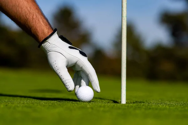 Golfer man hand met golfhandschoen. Golfbal bij het gat. Golfbal op lip van beker op gras achtergrond. — Stockfoto