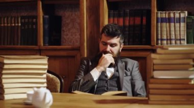 Kitaplık arka planında sakallı, kitap okuyan otantik bir adamın portresi. Yakışıklı, iyi giyimli bir adam klasik iç mimarisi olan bir odada kitaplığın yanında duruyor. Hukuk ve adalet kavramı.