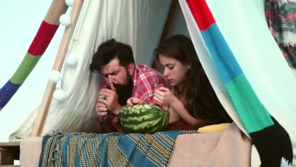 Romantic couple camping outdoors and sitting in a tent. Happy Man and woman on a romantic camping vacation. Friends eating watermelon. — Vídeo de stock