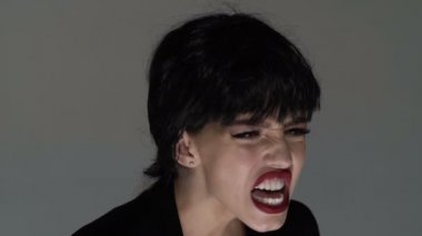 Çığlık, nefret, öfke. Gri stüdyo arka planında bağıran duygusal sinirli kadın. Duygusal, genç yüz. İnsani duygular, yüz ifadesi kavramı.