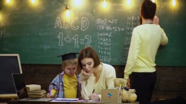 Evde oynayan bir aile. Ebeveynler çocuklarına ev ödevlerinde yardım ediyorlar. Genç bir anne ve baba oğullarının oturma odasında çalışmasına yardım ediyor. İlkokuldaki öğrenci çocuklar..
