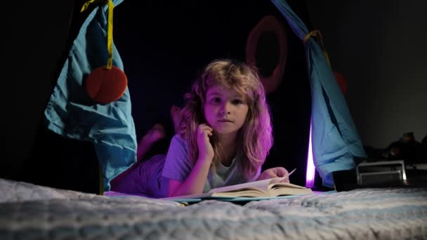 Niño en tienda de campaña para niños leyendo un libro en la cama antes de irse a dormir. Niño leyendo un libro a la hora de acostarse. Niño leyendo cuento de la hora de acostarse, cuento de hadas. — Vídeos de Stock