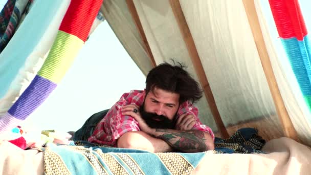Young bearded hipster in tent, dreaming. Romantic guy camping outdoors near tent. — Vídeos de Stock