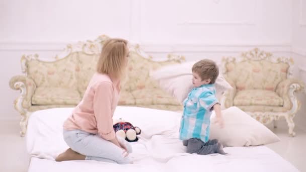 Mor med liten son som leker i sängen på helgen tillsammans, lat morgon. Mamma och barn pojke hoppa på en säng och ha kul slåss med kuddar. — Stockvideo