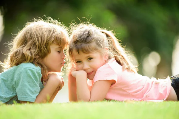 Adorable happy kids outdoors on summer day, little boy kissing a girl. Lovely little boy and girl, have fun outdoor, laying on grass. Funny kids face. Lovely children. First love. — 스톡 사진