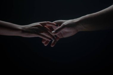 İki el birbirini gerer, siyah arka plan. Birbirine aşık çiftler, yaklaşın. Yardım eli, destek, arkadaşlık.