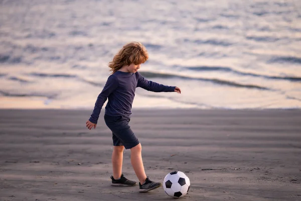 Young soccer player in sportswear with soccer ball. Cheerful little boy enjoy soccer, football sport games on sunset beach. —  Fotos de Stock