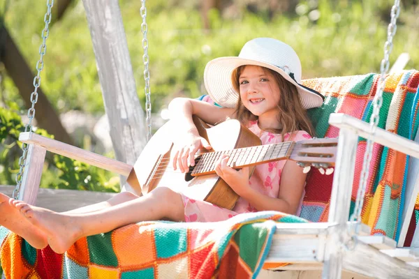 Gitar çalan müzisyen çocuk. Kız dışarıda gitar çalıp şarkı söylüyor. Sıcak havalarda çocuklar için yaz etkinliği. Şirin küçük kız güzel bir yaz bahçesinde salıncakta eğleniyor.. — Stok fotoğraf