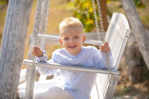 Glücklicher Junge lachend und auf einer Schaukel im Sommergarten schaukelnd. Frühlings-Kinderporträt. Kid Emotions Konzept. Porträt eines lachenden Jungen im Freien. — Stockfoto