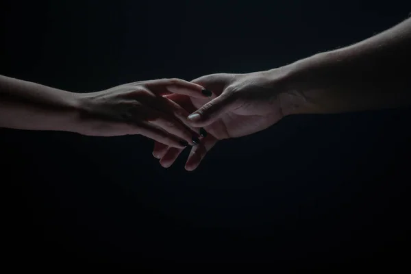 Duas mãos esticam-se umas às outras, fundo preto. Casal apaixonado segurando chapéus, de perto. Ajudando a mão, apoio, amizade. — Fotografia de Stock