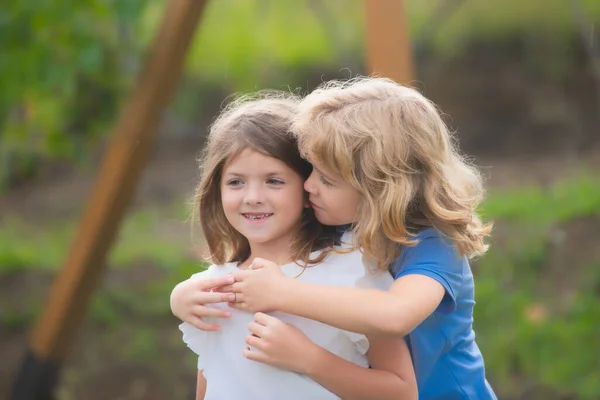 Kleiner Junge umarmt schüchternes Mädchen, kleiner Junge umarmt depressives kleines Mädchen, Beziehung, Freundschaftskonzept. Kinder im Freien umarmen. Schöne Kinder. Erste Liebe. — Stockfoto