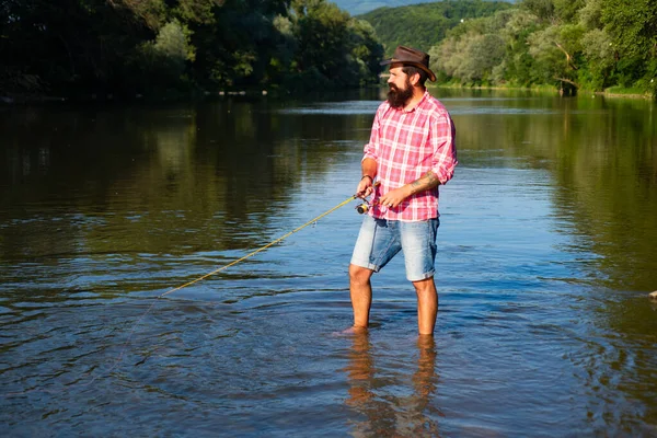Young bearded man fishing at a lake or river. Flyfishing. — Stock Photo, Image