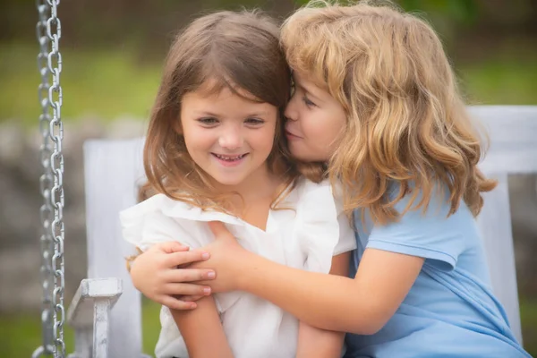 Dos niños pequeños se abrazan y se besan en el jardín de verano. Pareja de niños enamorados. Amistad e infancia. Niños felices divirtiéndose al aire libre. Niños jugando en el parque de primavera. Chica tímida. —  Fotos de Stock