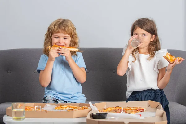 Hungry children eating pizza. Two young children bite pizza indoors. — Foto de Stock
