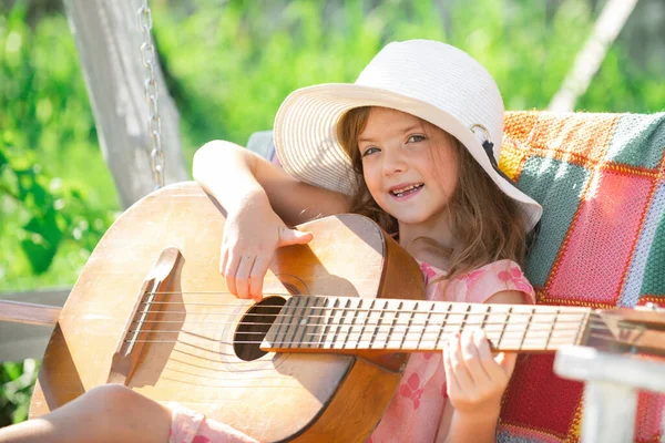 Çocuk müziği ve şarkıları. Gitar çalan küçük bir çocuk. Moda kızı. Çocuk müzik gitar okulu. Gülümseyen çocuk yazın dışarıda oynuyor.. — Stok fotoğraf