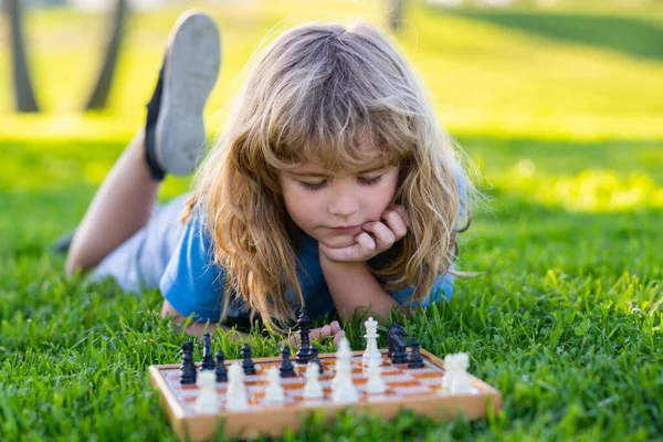 Little clever boy thinking about chess. Kid playing chess, laying on grass in summer park. — Stock Photo, Image