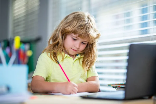 Een kind dat huiswerk schrijft in de klas. Schooljongen maakt notities in het copybook tijdens online les op laptop thuis. Leuke jongen die huiswerk maakt. Kinderonderwijs. — Stockfoto
