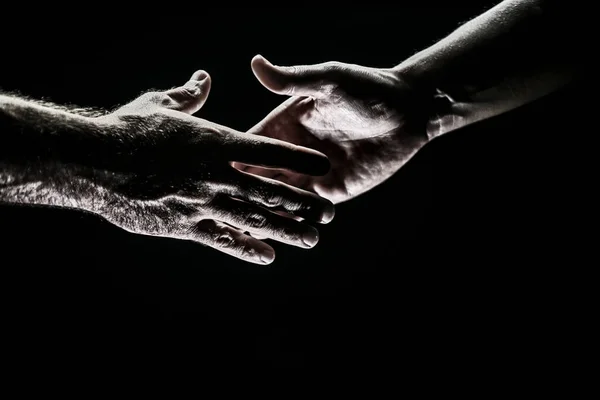 Un apretón. Hombres tomados de las manos aislados en negro. Conexión y relaciones humanas. Rescate manos masculinas. Un apretón de manos amistoso, saludo de amigos, amistad. Rescate, ayuda gesto o manos. Mano de ayuda. —  Fotos de Stock
