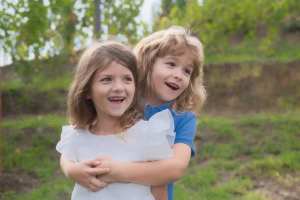 Junge und Mädchen umarmen sich. Zwei kleine Kinder, Bruder und Schwester, die sich im Park umarmen. Freunde von Kindern spielen zusammen im Freien. — Stockfoto
