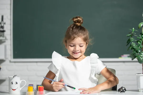 Öğrenci resim öğreniyor. Boya rengi ve fırçayla resim yapan şirin bir kız çocuğu. Okulda resim dersi.. — Stok fotoğraf