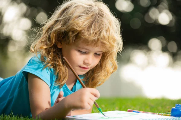 Child boy painting with paints color and brush in park outdoor. Happy child playing outside. Drawing summer theme. Imagination kids concept. Stock Photo