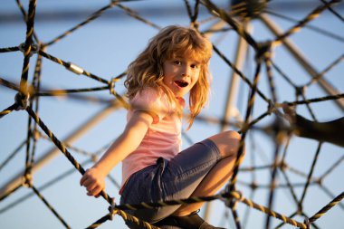 Çocuk ağa tırmanıyor. Çocuk çocuk oyun parkındaki halat ağına tırmandı. Çocuklar güneşli yaz gününde dışarıda oynar ve tırmanırlar..