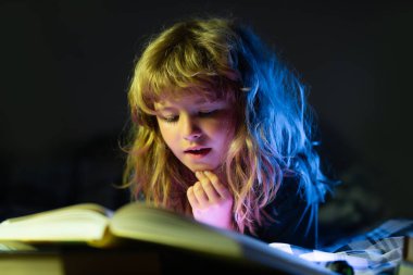 Çocuk uyumadan önce yatakta kitap okuyor. Evdeki küçük çocuk yatakta uzanıp kitap okuyor. Çocukların hayal gücünün gelişimi..