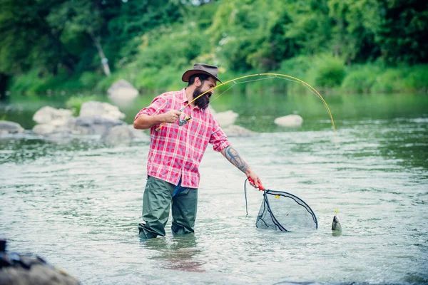 Mladý muž rybaří. Rybář s prutem, točí se navijákem na břehu řeky. Chlap chytající ryby, tahající prut při rybaření na jezeře. Divoká příroda. Koncept úniku z venkova. — Stock fotografie