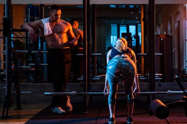 Spor salonunda halterli çift eğitimi. Halterli kadın çalıştıran kaslı antrenör..