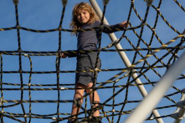 Çocuk çocuk oyun parkındaki halat ağına tırmandı. Çocuk ağa tırmanıyor. Çocuklar güneşli yaz gününde dışarıda oynar ve tırmanırlar..