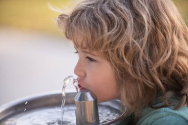 Parktaki çeşmeden su içen bir çocuk. Susamış çocuk.