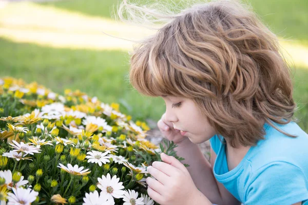 Tavaszi gyerek arc. Közelkép egy kis szőke fiúról tavaszi virággal. Vicces kölykök a kertben. A gyerekek összezárják arcukat a virágos háttérrel. Gyermek lány játszani tavaszi virágok. — Stock Fotó