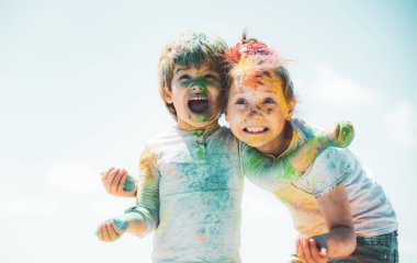 Mutlu çocuklar renkli holi tozuyla oynuyorlar. Sevimli anaokulu öğrencileri kucaklaşırken kameraya bakarlar..