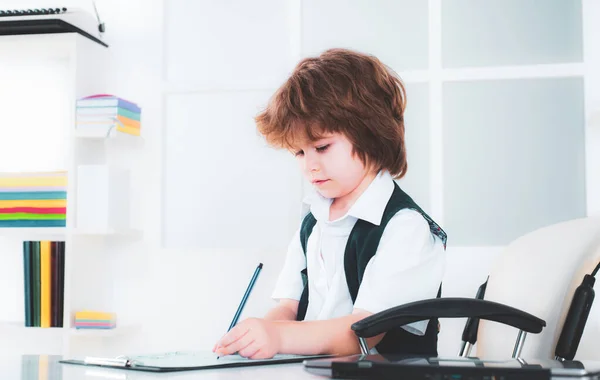 Porträtt av en liten pojke som sitter vid sitt skrivbord på kontoret. Barnaffärsman vid sitt skrivbord. Tråkigt jobb.Ung affärsman. — Stockfoto