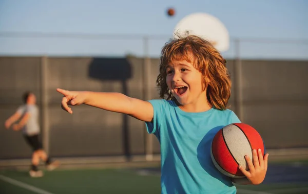 Słodki chłopiec gra w koszykówkę, pokazując gest. Aktywne dzieci korzystających z odkrytej gry z piłką do koszykówki. — Zdjęcie stockowe