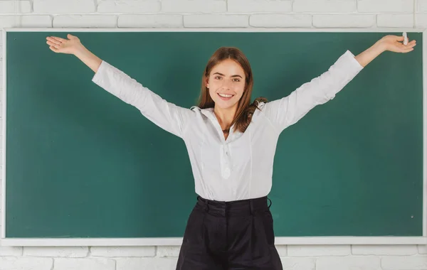 Estudiante emocionado estudiante amazet con las manos levantadas sosteniendo tiza en el aula de la escuela en el fondo de pizarra. —  Fotos de Stock