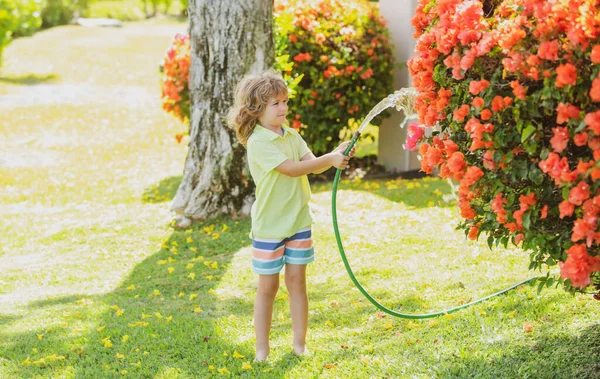 Счастливый мальчик наливает воду из шланга. Детство американских детей. Дети поливают цветы в саду. Садоводство. — стоковое фото