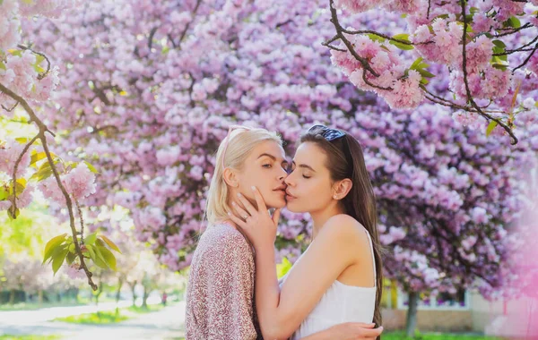 Tavaszi lányok. Leszbikus pár csókolózik. Gyönyörű tavaszi szexi lány szakura virágokkal. Érzelmi csók. A barátnők szeretnek.. — Stock Fotó