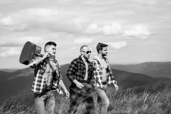 Τρεις ευτυχισμένοι φίλοι κοιτάζουν στα βουνά και διασκεδάζουν μαζί. Ομάδα φίλων σε περίπατο στην εξοχή μια καλοκαιρινή μέρα. Περιπέτεια άνδρες και γυναίκες πεζοπόροι αναρρίχηση στο βουνό γκρεμό κάτω από τον ουρανό. — Φωτογραφία Αρχείου