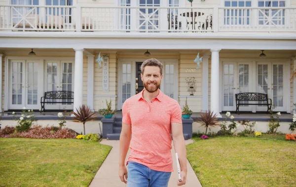 Retrato de agente imobiliário confiante em pé fora de uma casa para venda. Um agente imobiliário à espera de visitas. Confiança e conceito de negócio. Retrato de encantador empresário bem sucedido em t-shirt. — Fotografia de Stock